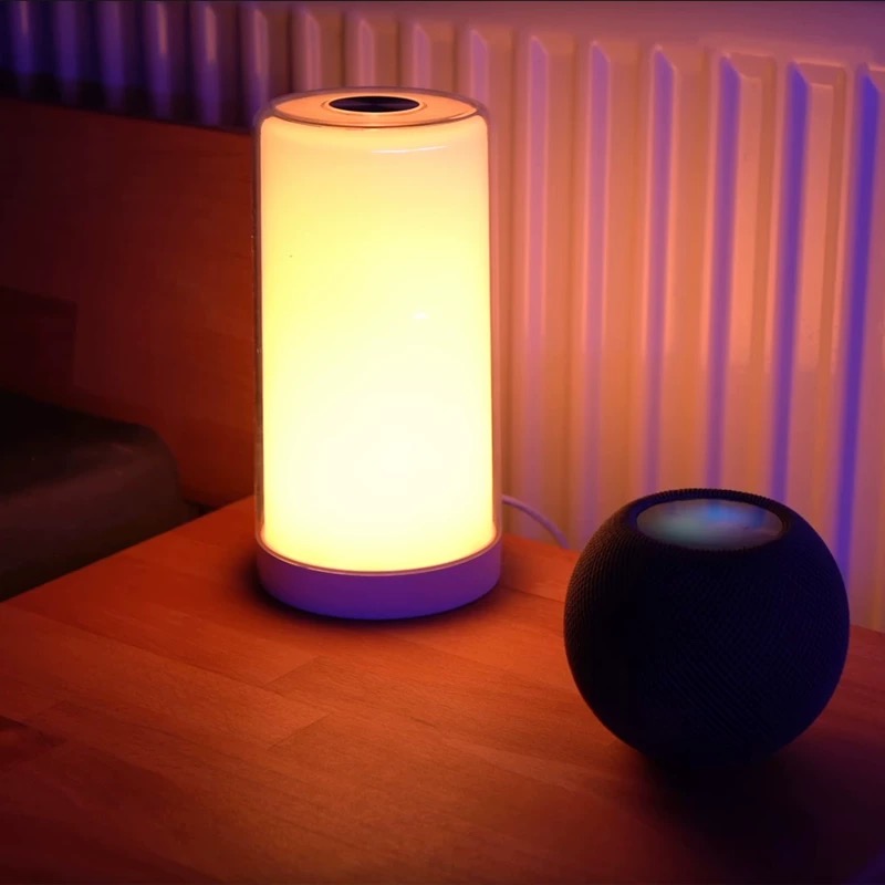 Meross MLS430 智慧觸控床頭燈，亮著暖色調的黃光，照亮了一起放在床頭櫃上的 HomePod Mini。